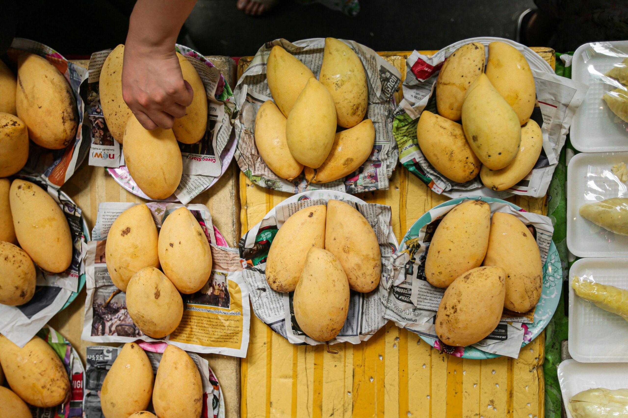 Ripe mangoes arranged on plates at a vibrant market stall, seen from above.